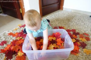 Autumn leaves spilling out of a toddler sensory bin onto the floor