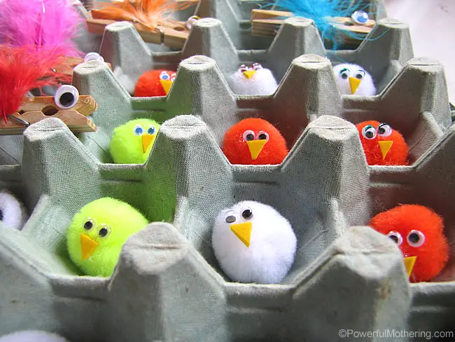 Pom pom baby birds with googly eyes sitting in an egg carton nest