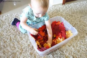 Toddler searching for acorns hidden in a leaf sensory bin